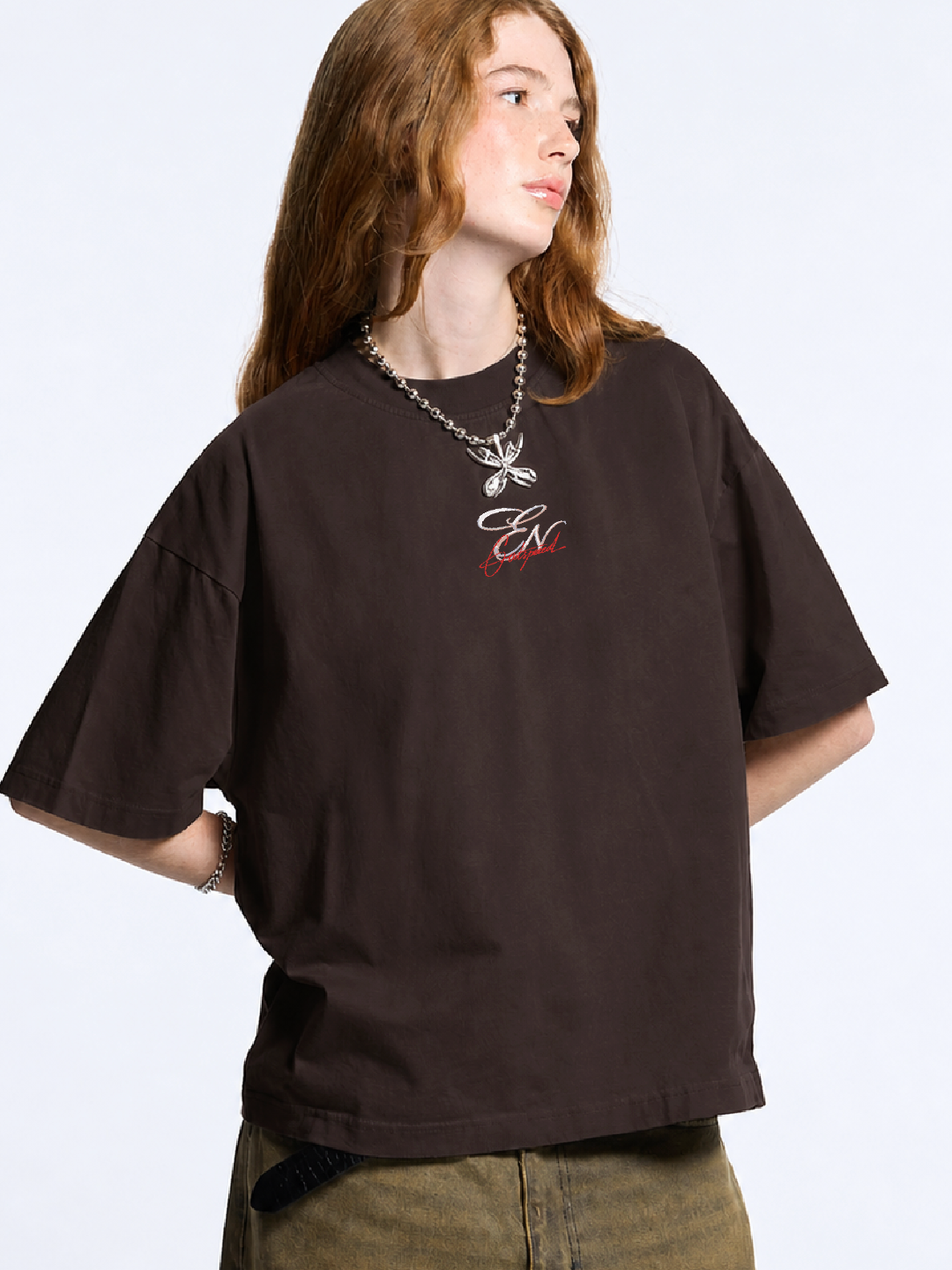 Person wearing a brown t-shirt with a logo on a plain background