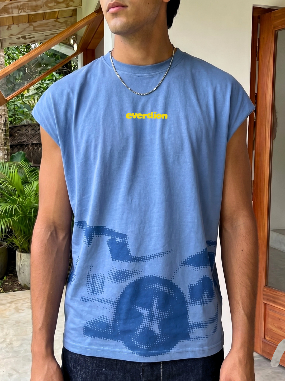 Person wearing a blue sleeveless shirt with a logo, standing outdoors.