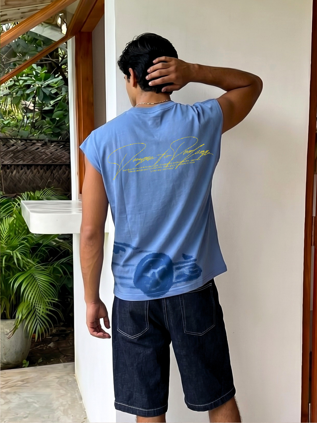 Person wearing a blue sleeveless shirt with text and graphics, standing against a white wall.