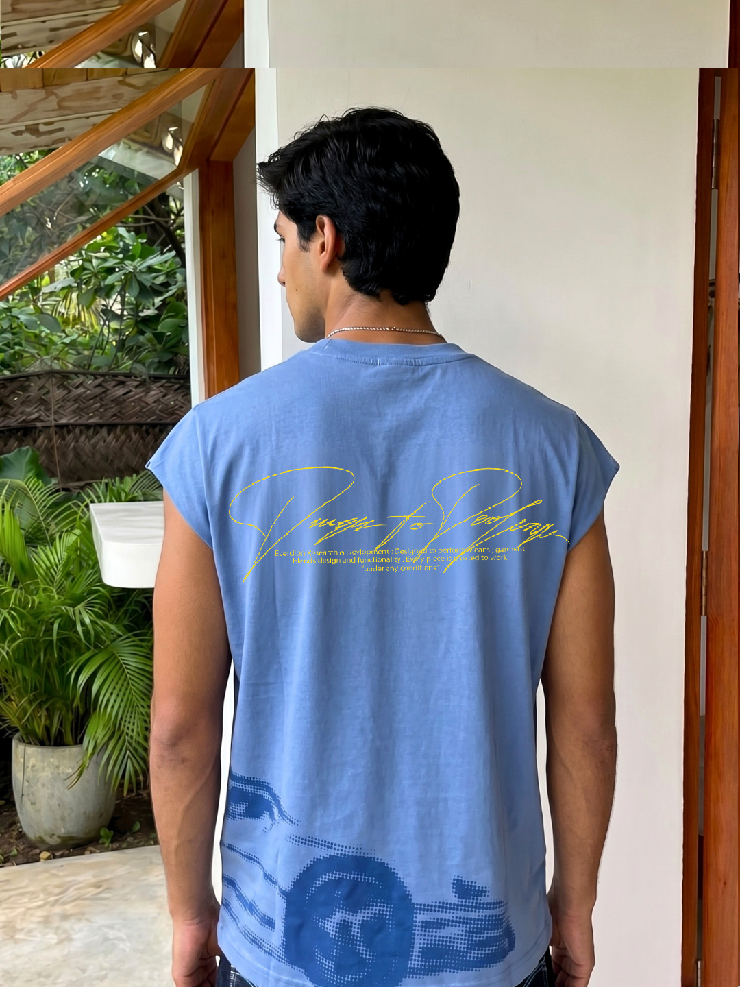 Man wearing a blue sleeveless shirt with text and graphics, standing outdoors.