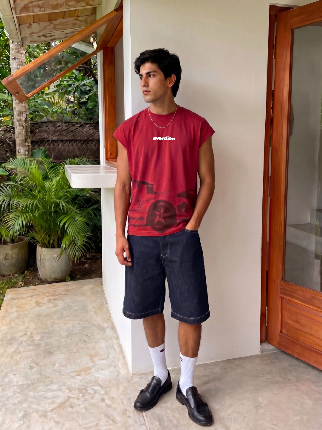 Person wearing a red t-shirt and dark shorts standing outside a house.