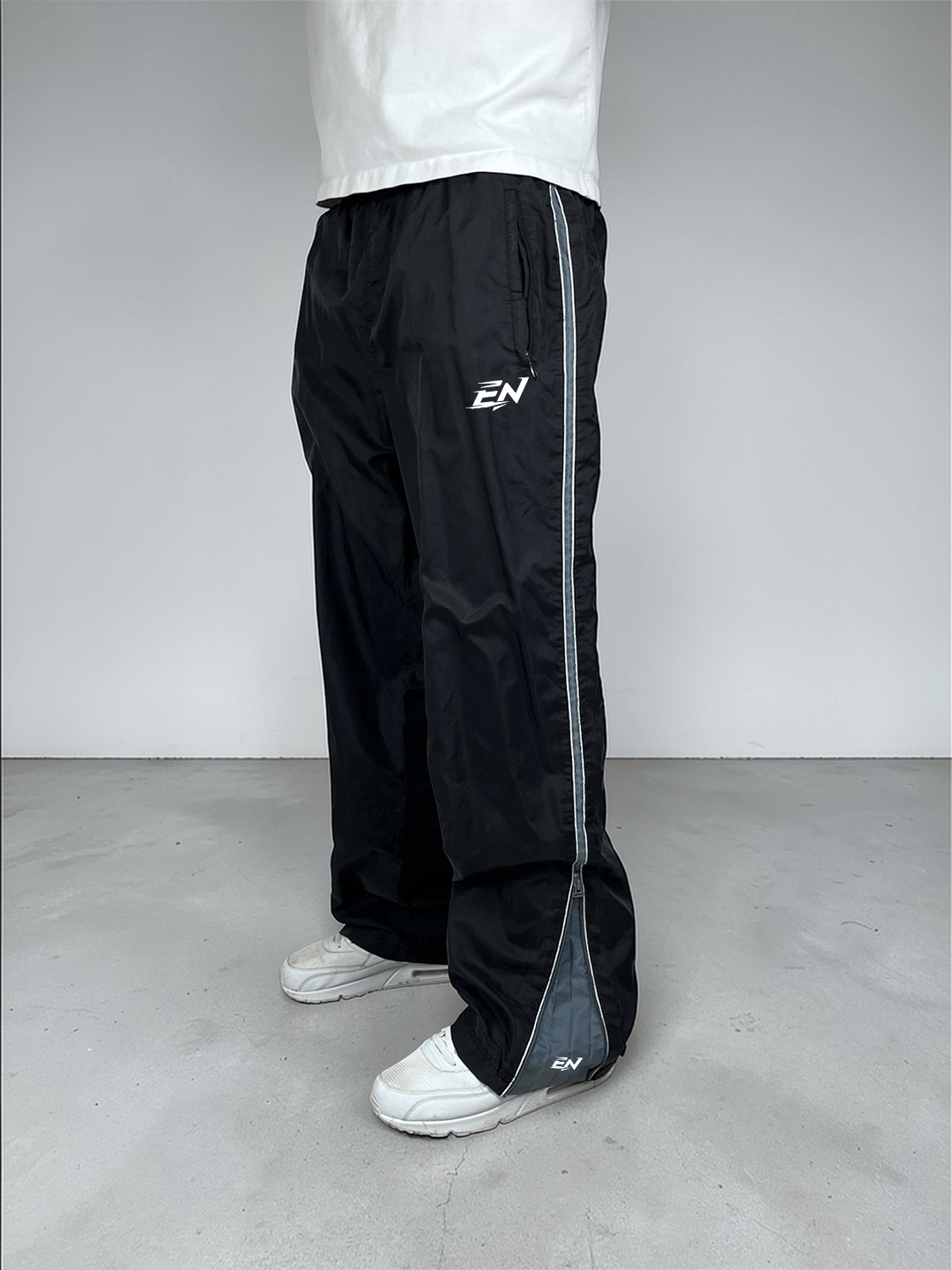 Person wearing black Nike pants with a white shirt and white shoes on a plain background