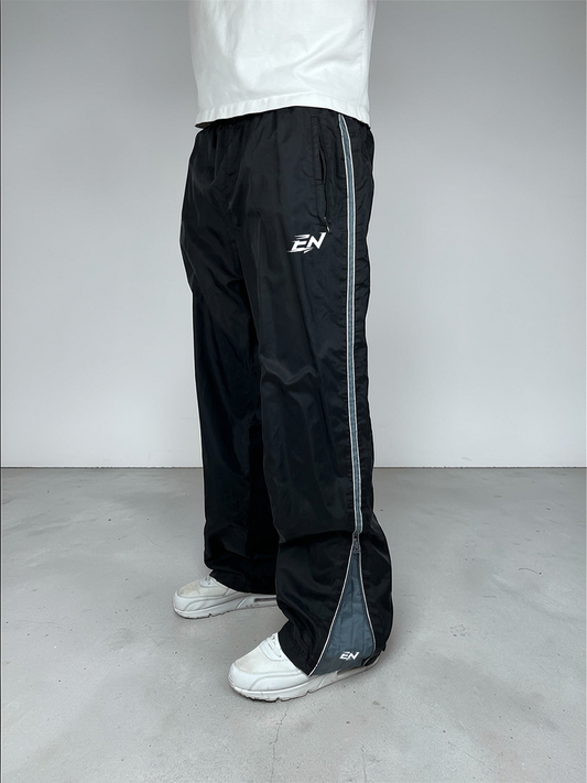 Person wearing black Nike pants with a white shirt and white shoes on a plain background