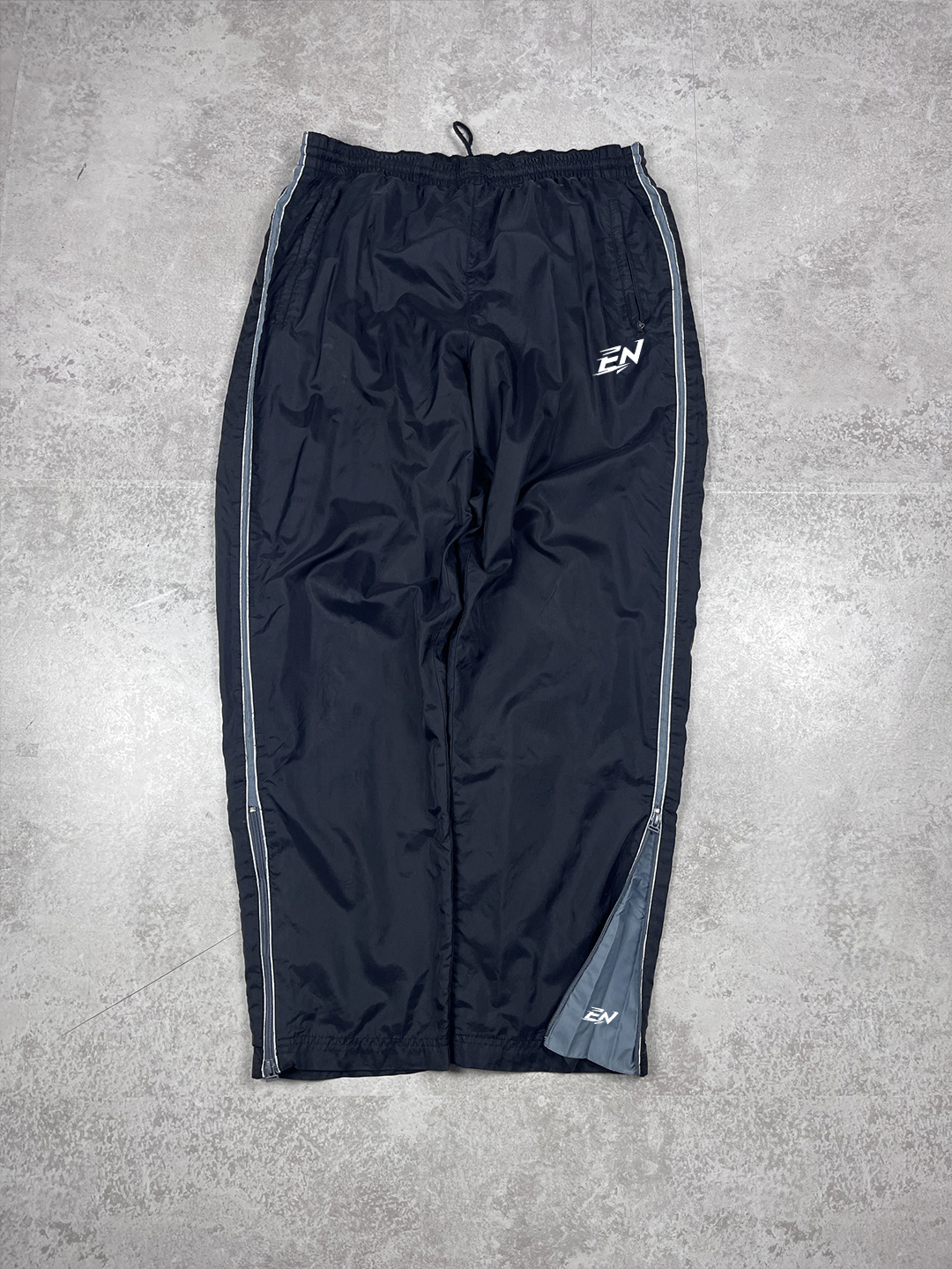 Black athletic pants with a logo on a grey concrete floor