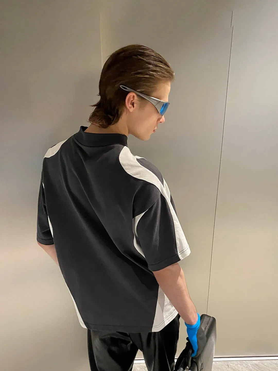 Person wearing a black and white shirt with blue sunglasses, standing against a plain wall.