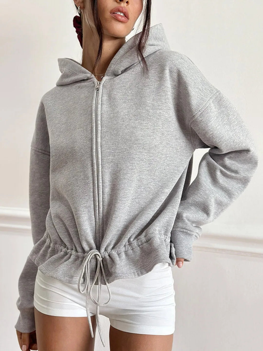 Person wearing a gray zip-up hoodie with a white background