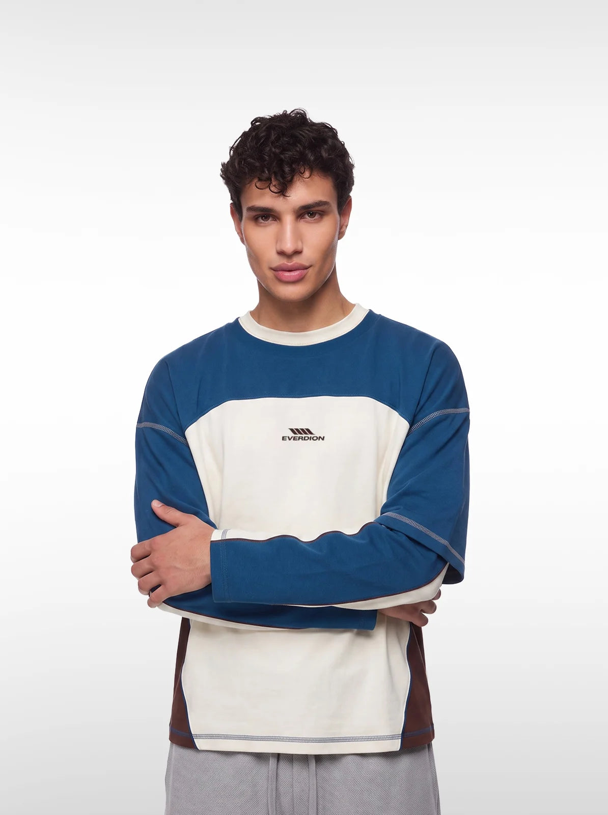 A man wearing a color-blocked long-sleeve tshirt with blue, cream, and brown panels