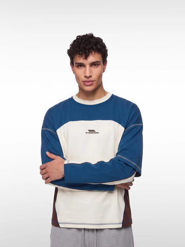 A man wearing a color-blocked long-sleeve tshirt with blue, cream, and brown panels