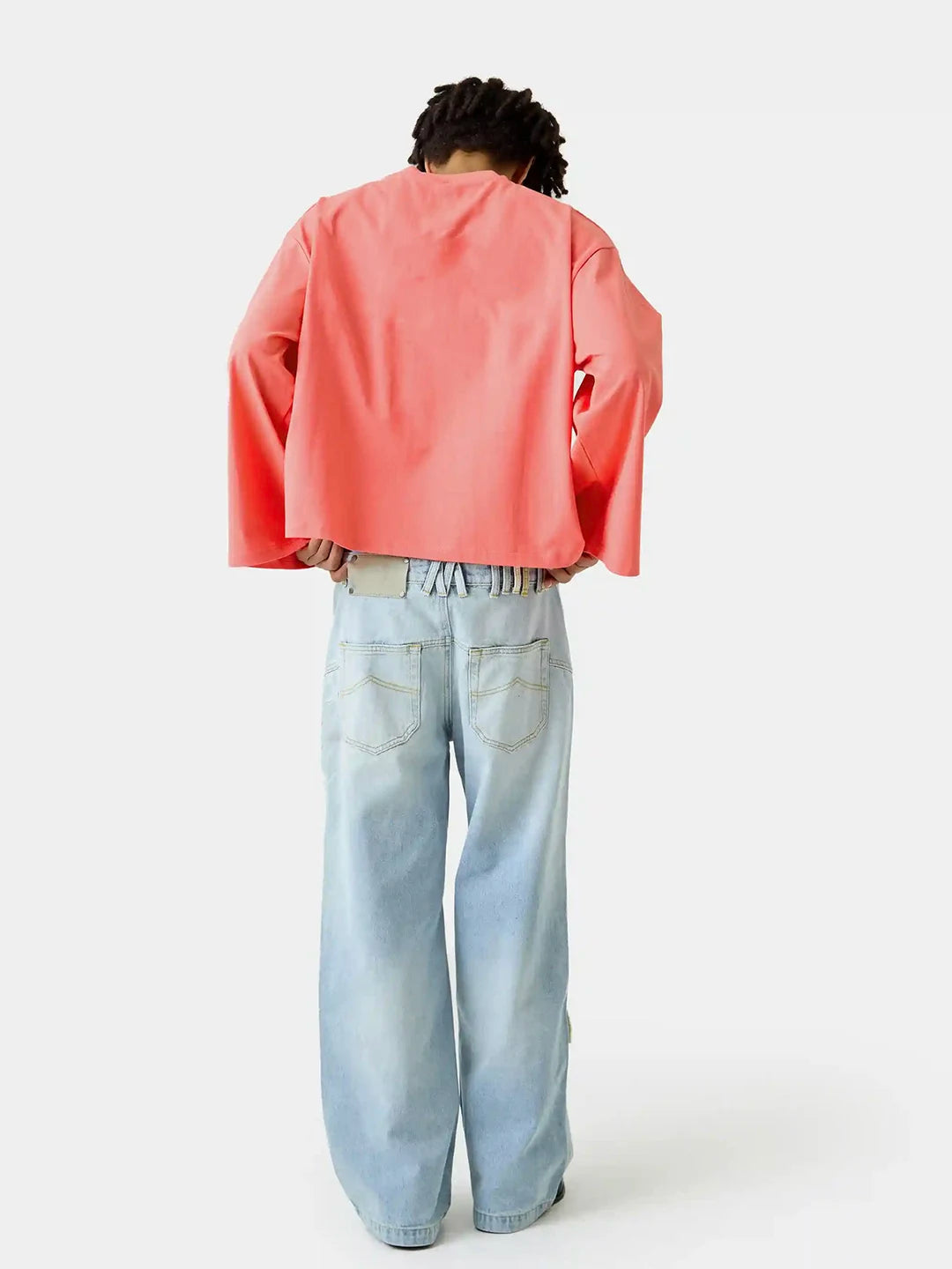 A model shown from the back wearing a coral pink cropped long-sleeve top and light blue wide-leg jeans against a plain white studio background.