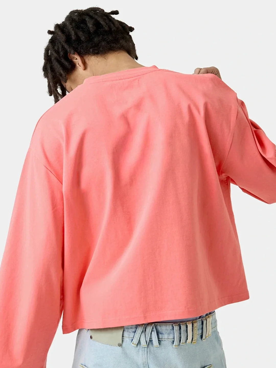 A person wearing a coral pink long-sleeve crop top and light blue jeans 