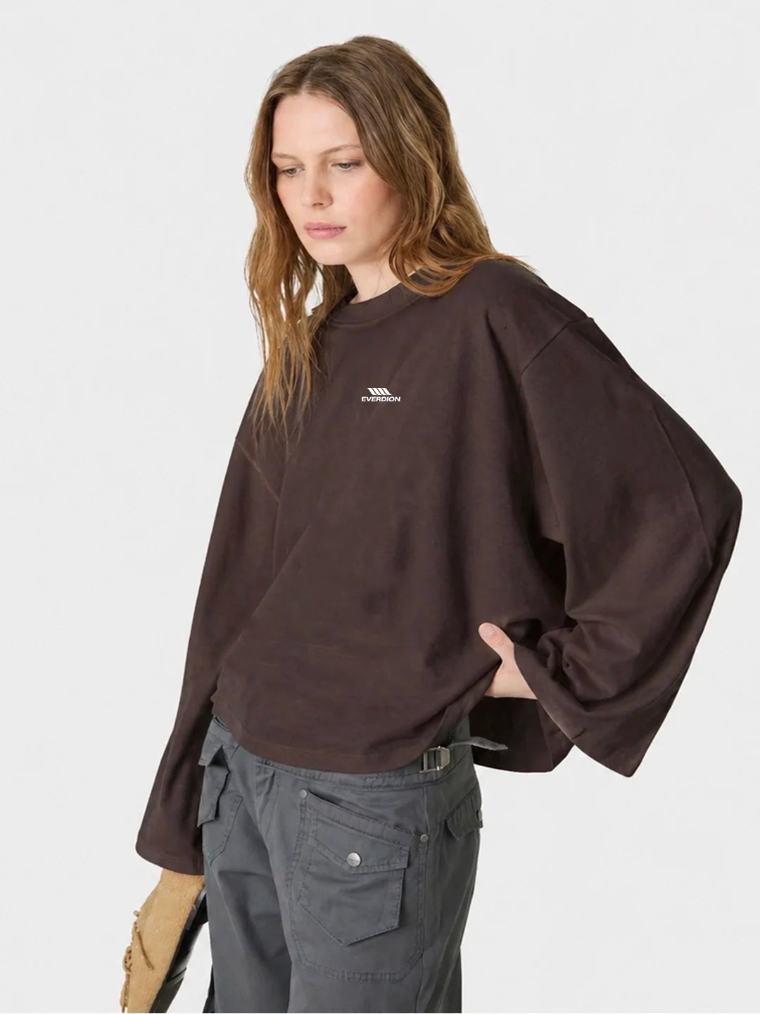 A woman wearing a dark brown oversized long-sleeve tshirt with a small white chest logo, paired with grey cargo pants, photographed 