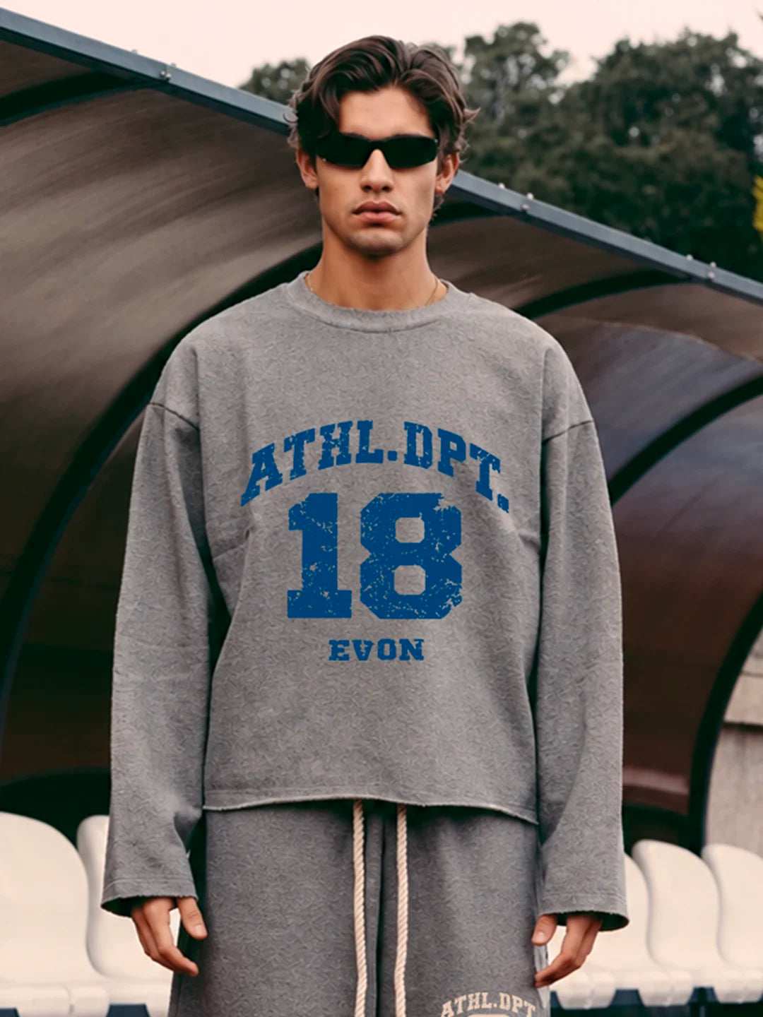 A man wearing an oversized grey tshirt with blue distressed text reading 'ATHL.DPT.