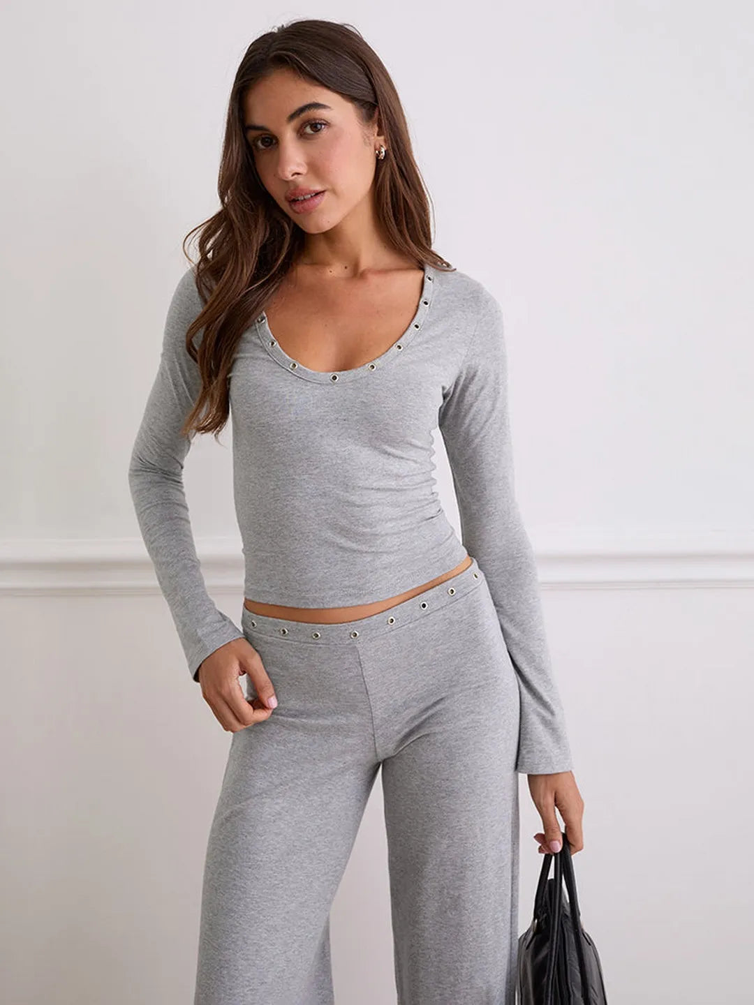 Woman wearing a gray long-sleeve top and pants against a white background