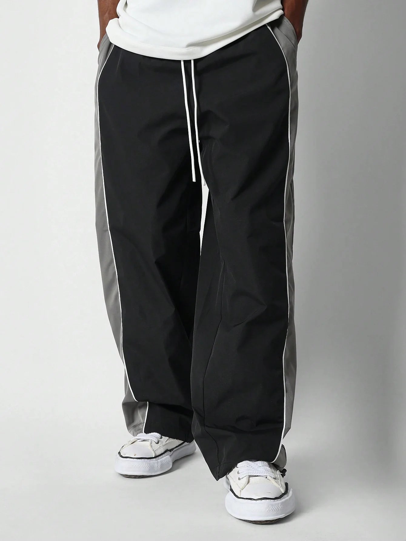 Person wearing black and grey track pants with white sneakers on a plain background