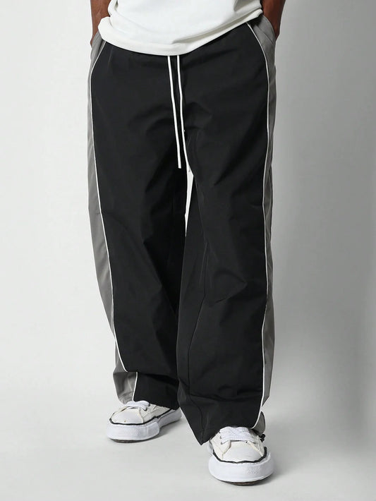 Person wearing black and grey track pants with white sneakers on a plain background