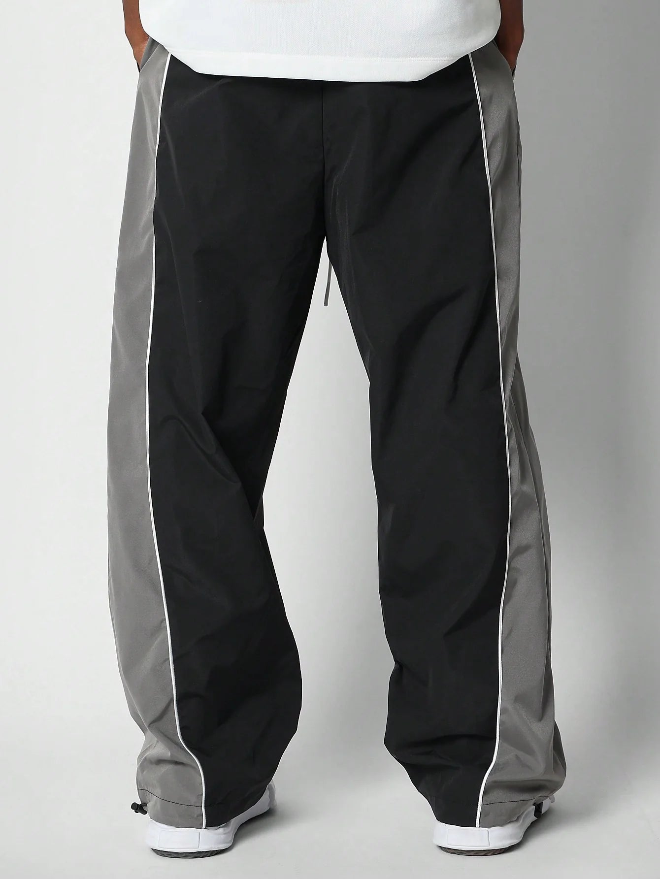 Black track pants with grey side panels on a plain background