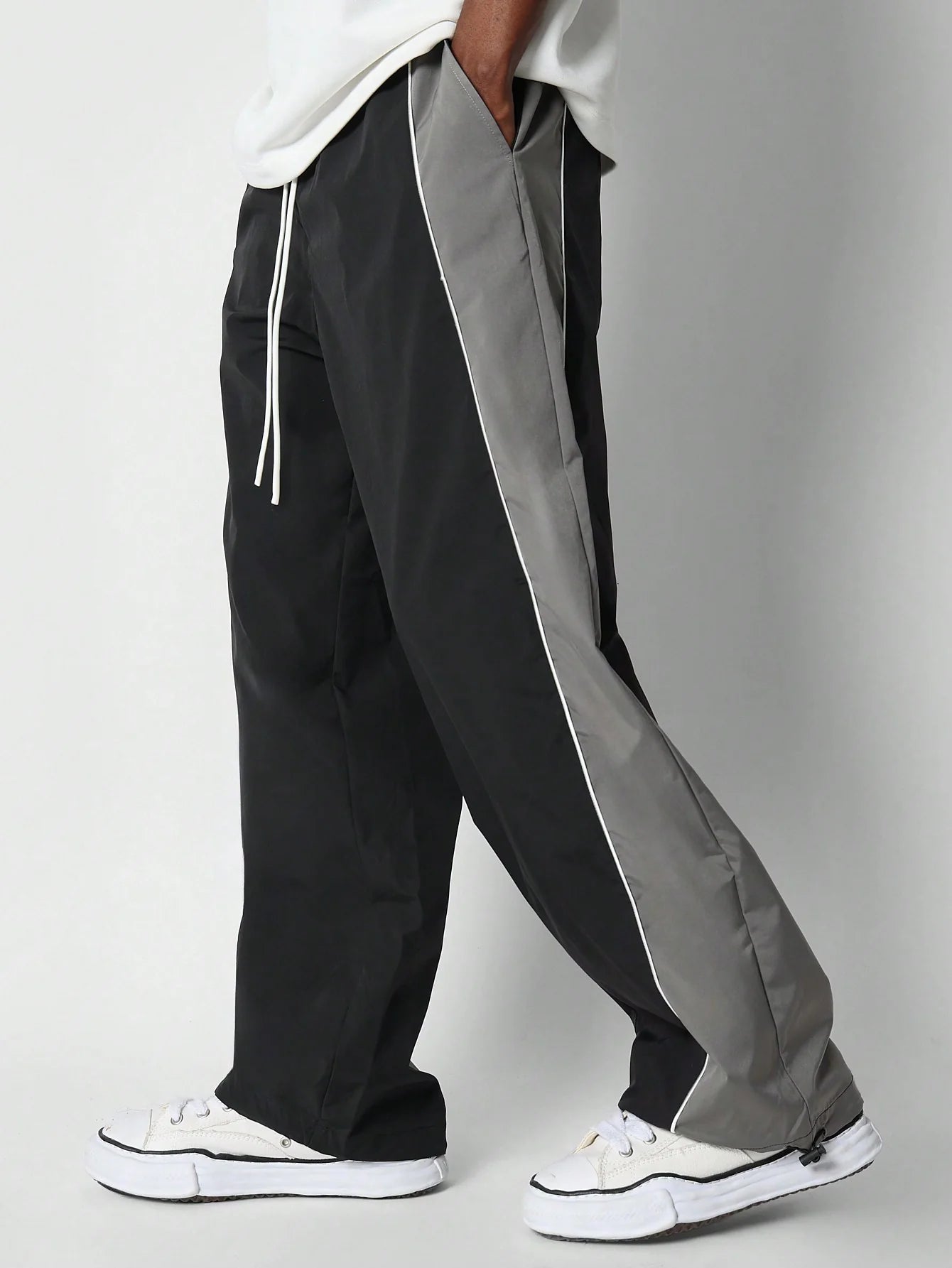 Black and grey track pants with white sneakers on a plain background