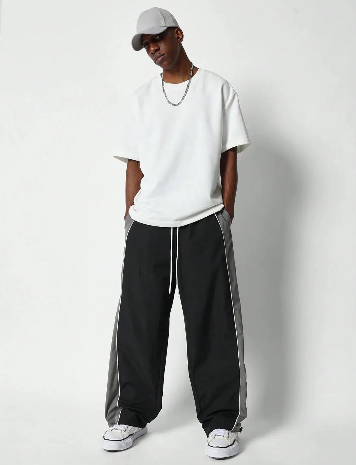 Person wearing a white t-shirt, black pants with grey stripes, and a cap on a white background