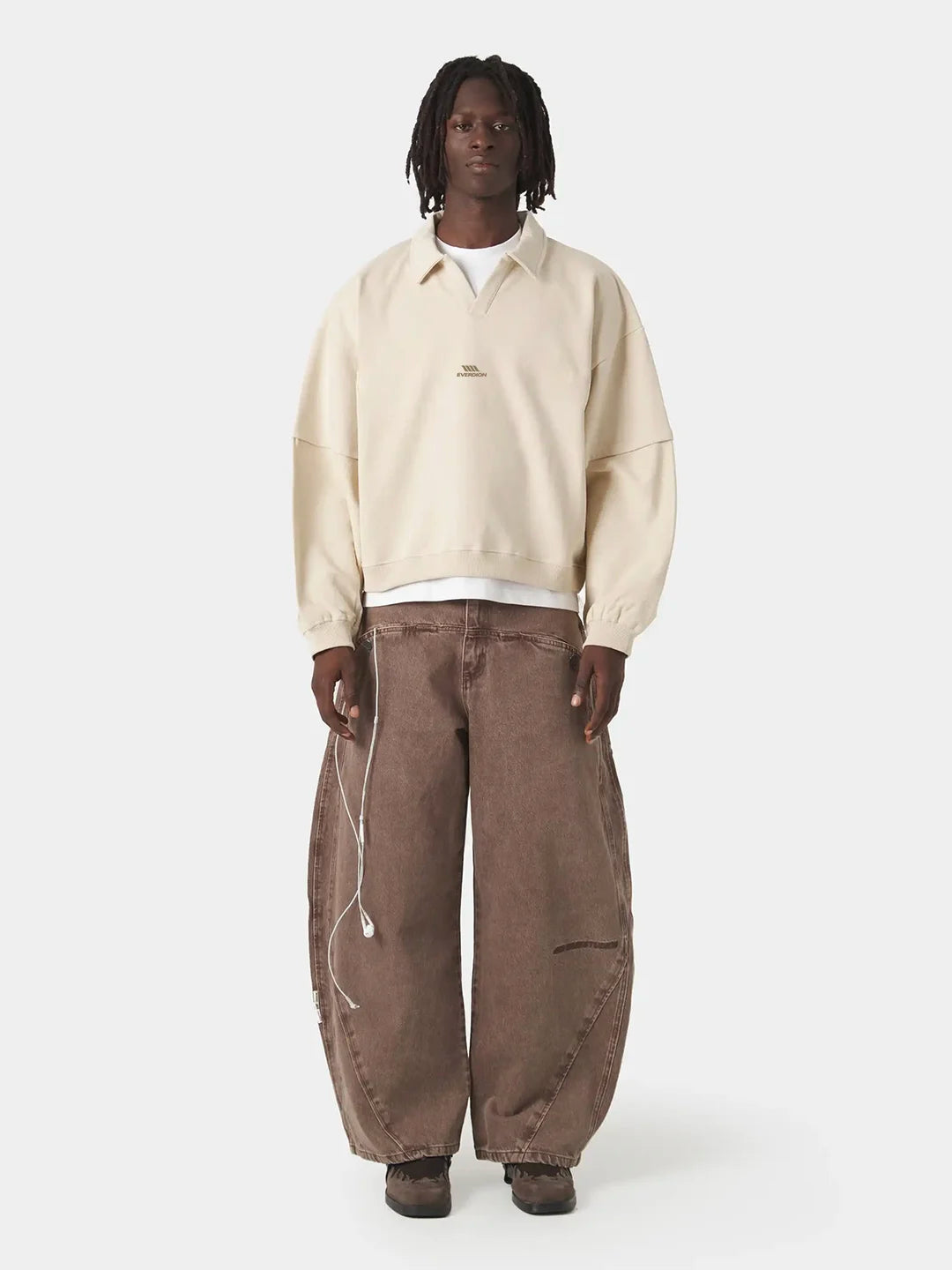 A person wearing a cream-colored cropped quarter-placket polo t-shirt, brown wide-leg cargo pants, and dark brown shoes.