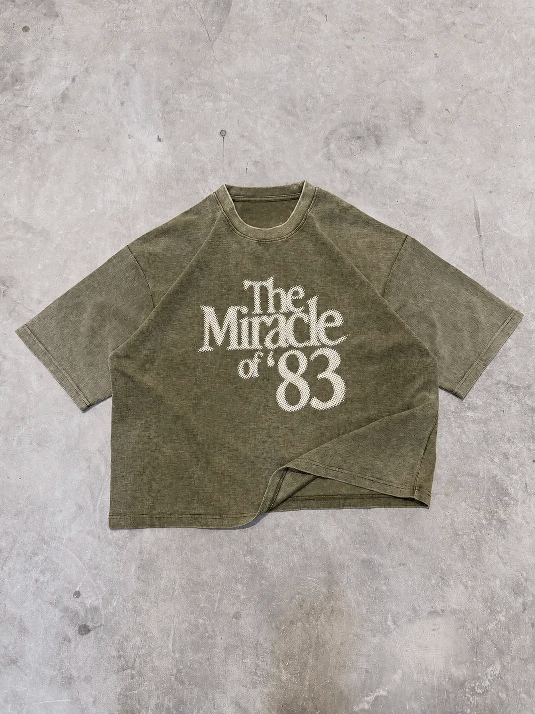 An oversized short-sleeve t-shirt in a washed olive green color, featuring the text 'The Miracle of '83' printed in white on the front. 