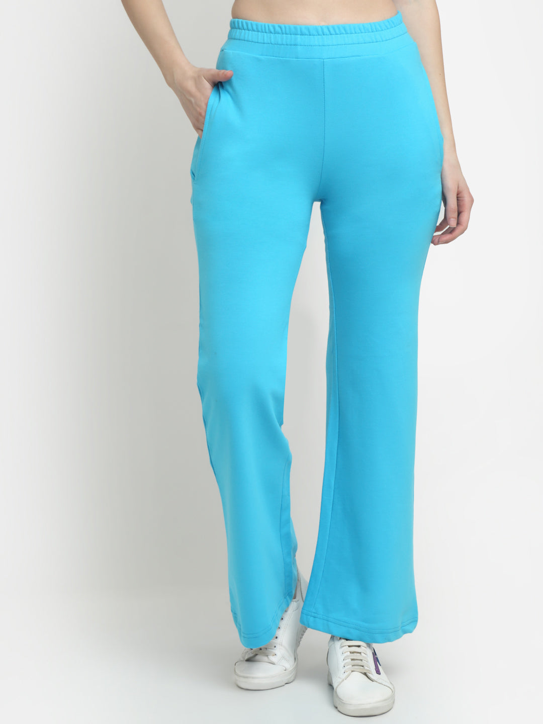 A pair of sky blue flared track pants on a female model, with the model's hands in pockets and wearing white sneakers.