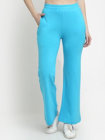 A pair of sky blue flared track pants on a female model, with the model's hands in pockets and wearing white sneakers.