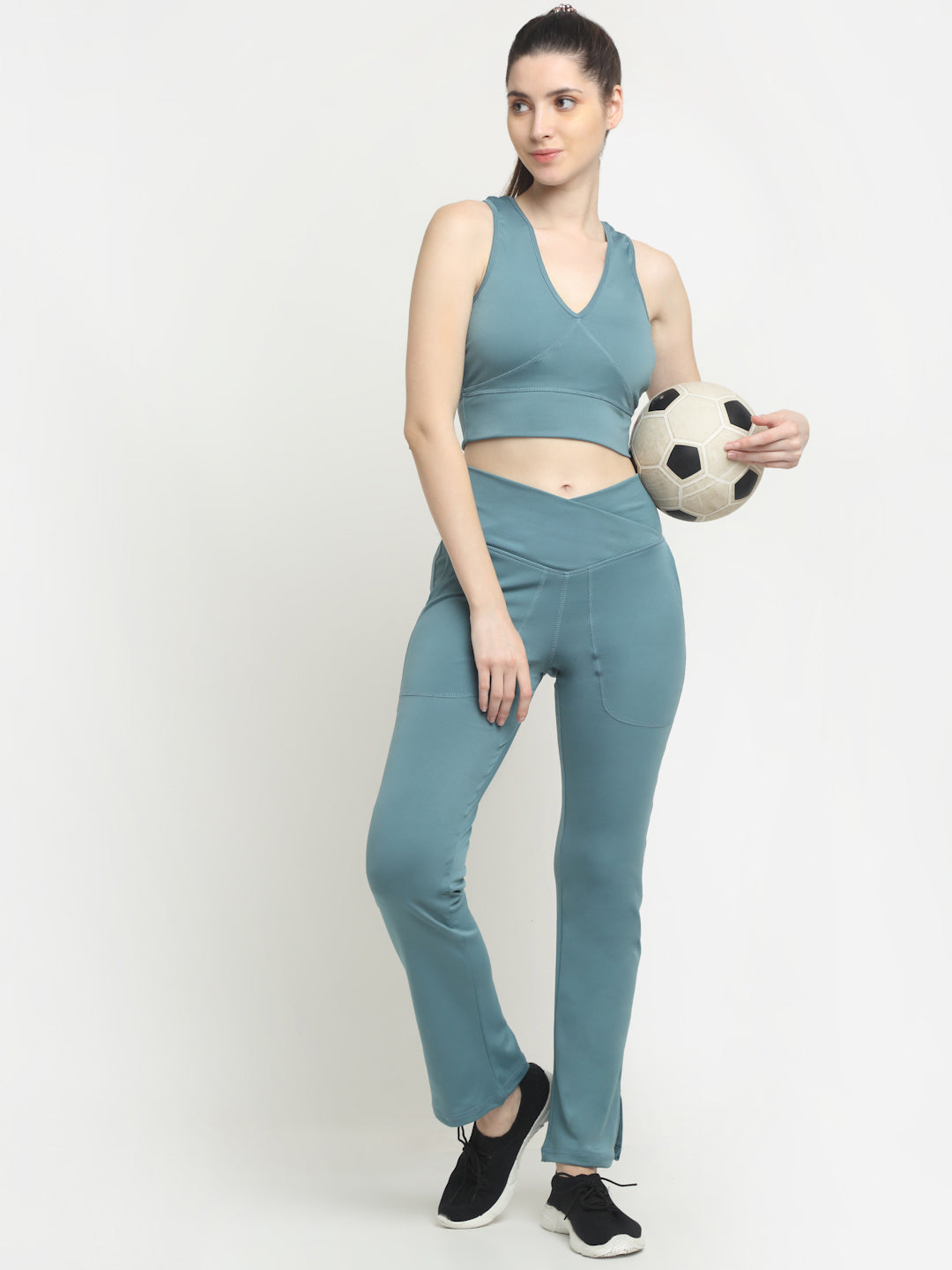 A woman standing and holding a soccer ball, wearing ice blue flare leggings with a crossover design and a sports top.