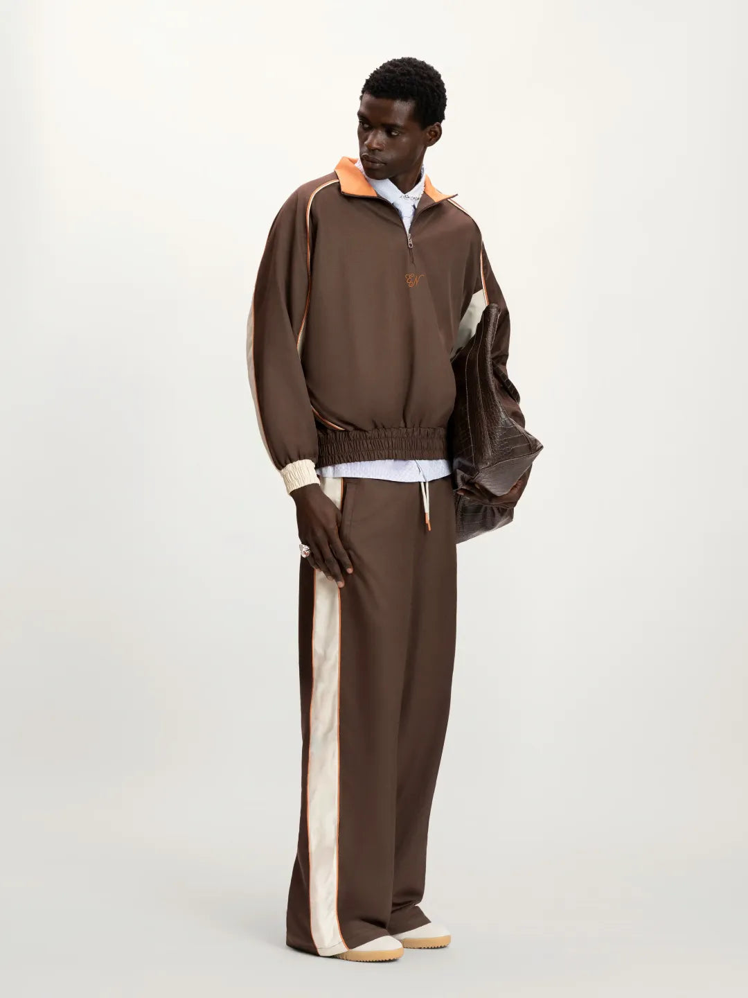 Man wearing a brown tracksuit with white accents on a white background