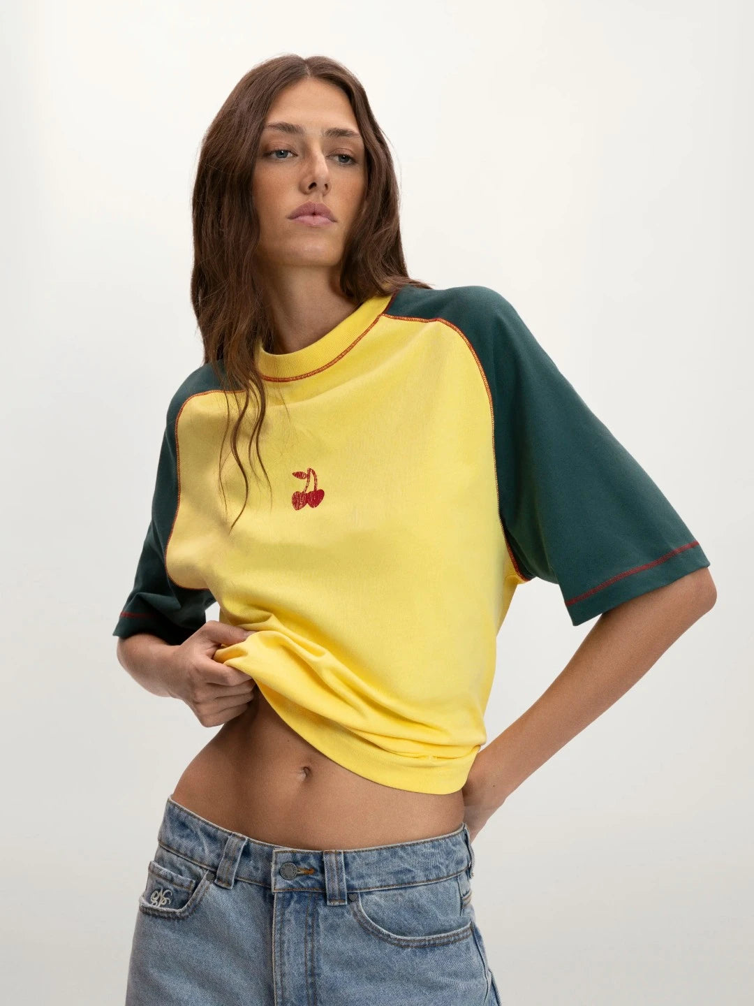 Woman wearing a yellow and green baseball shirt with a cherry design on a white background