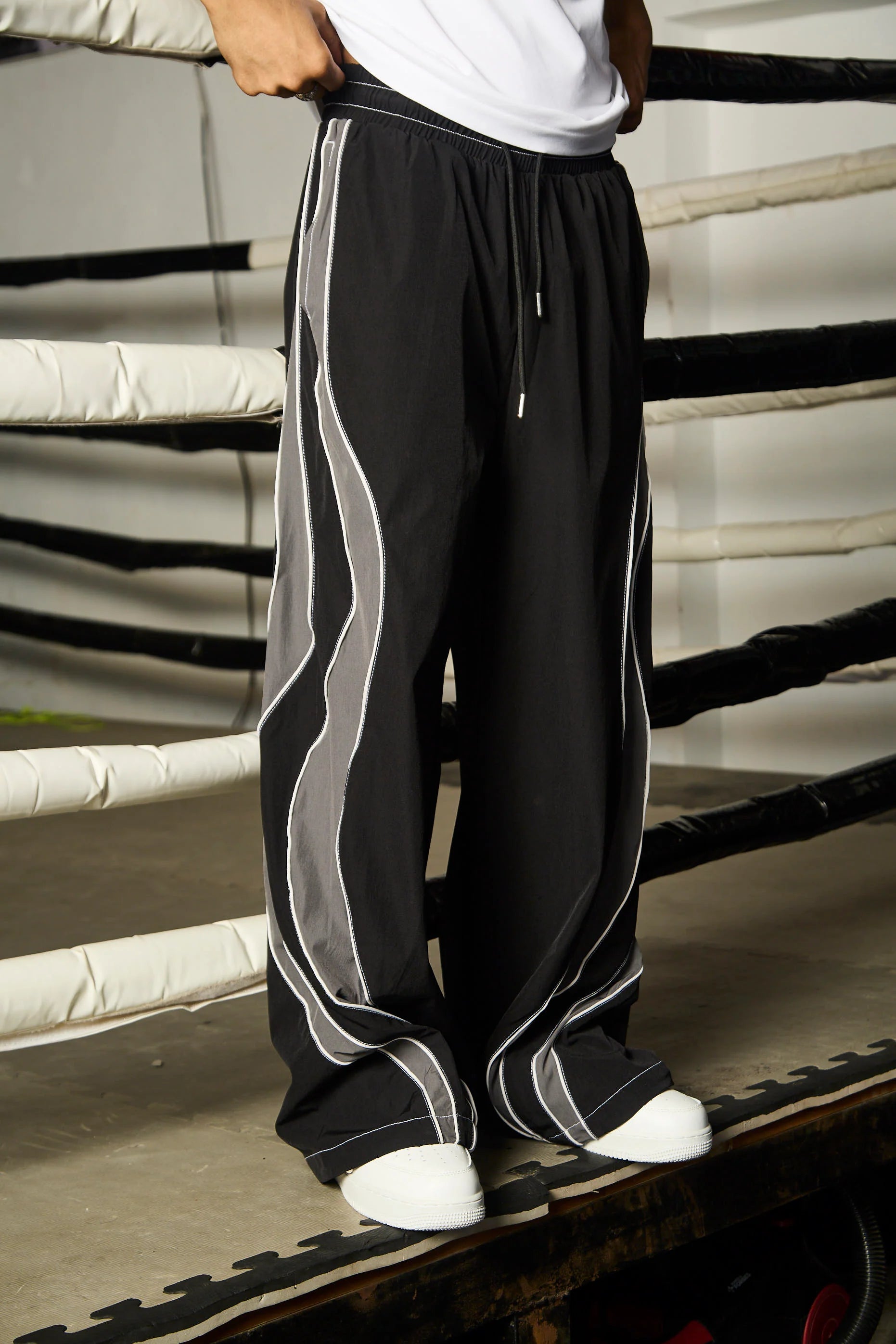 Person wearing black track pants with grey stripes standing on a wooden floor.