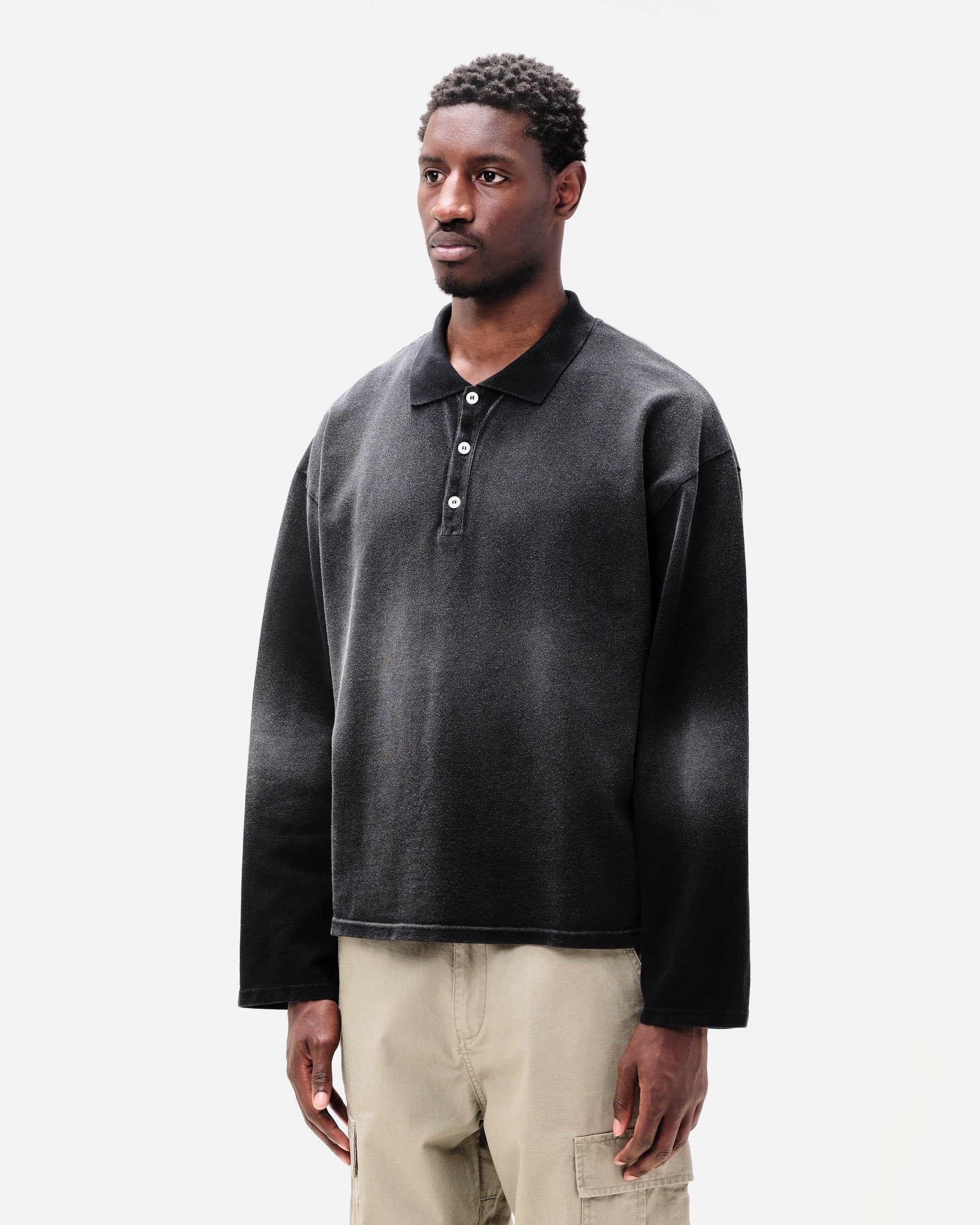 Man wearing a dark grey oversized polo shirt with beige pants on a white background