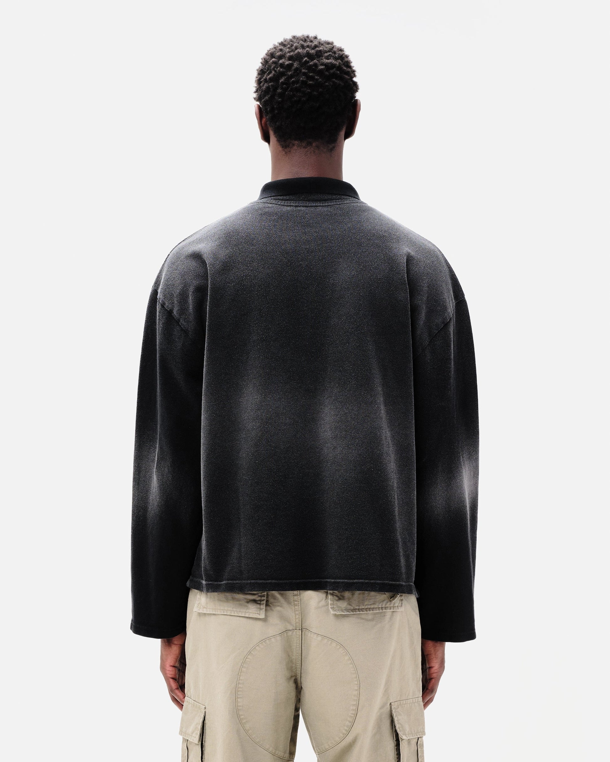 Man wearing a dark grey oversized polo shirt with beige pants on a white background