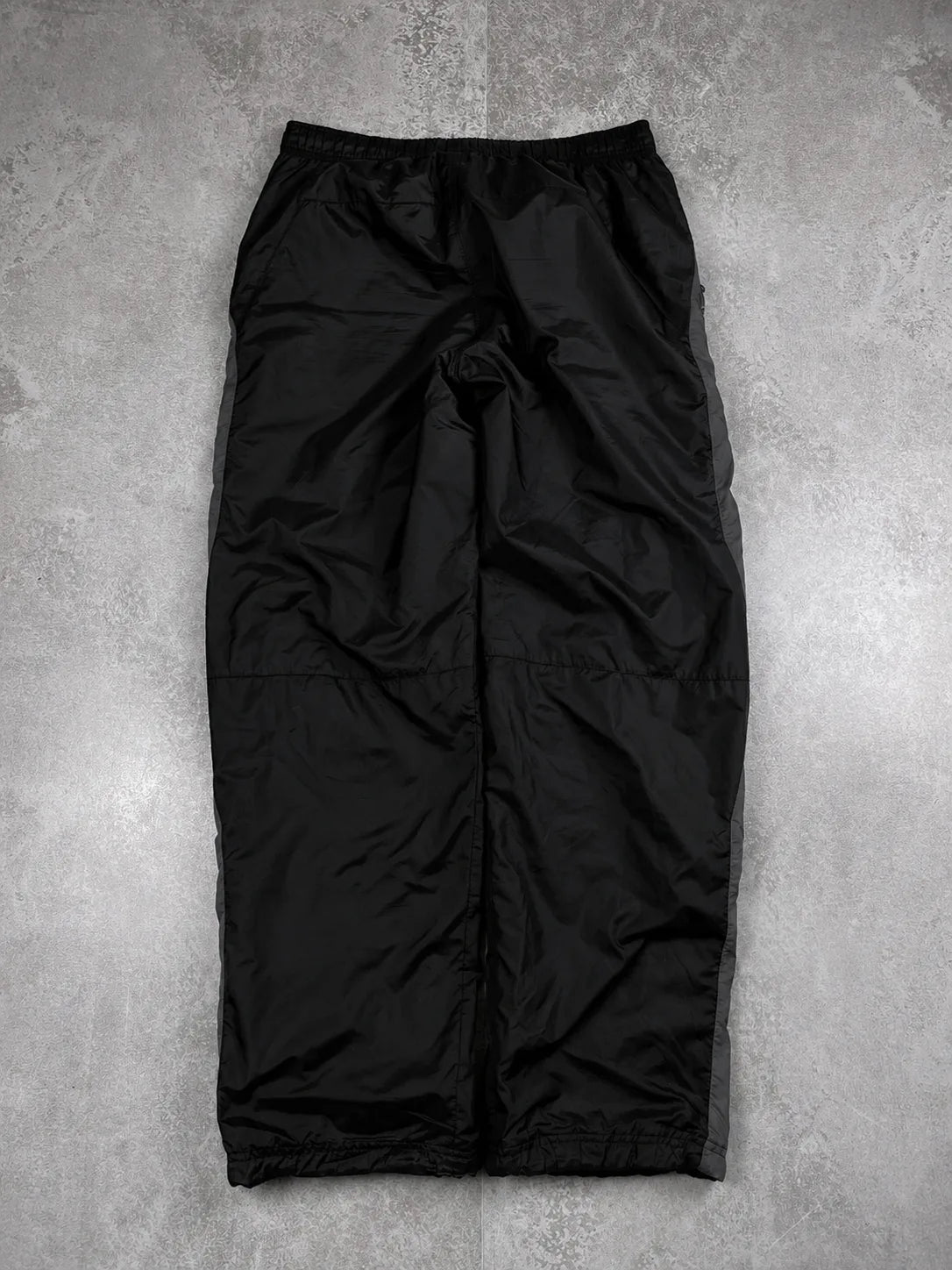 Black lightweight pants laid flat on a textured grey concrete surface.