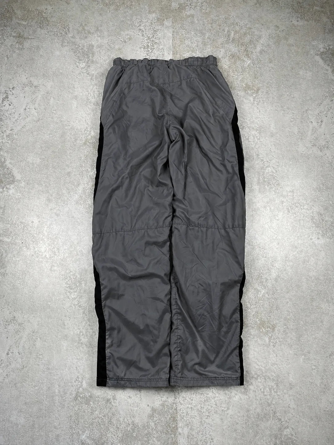 Dark grey waterproof pants with black side panels, laid flat on a textured grey concrete surface.