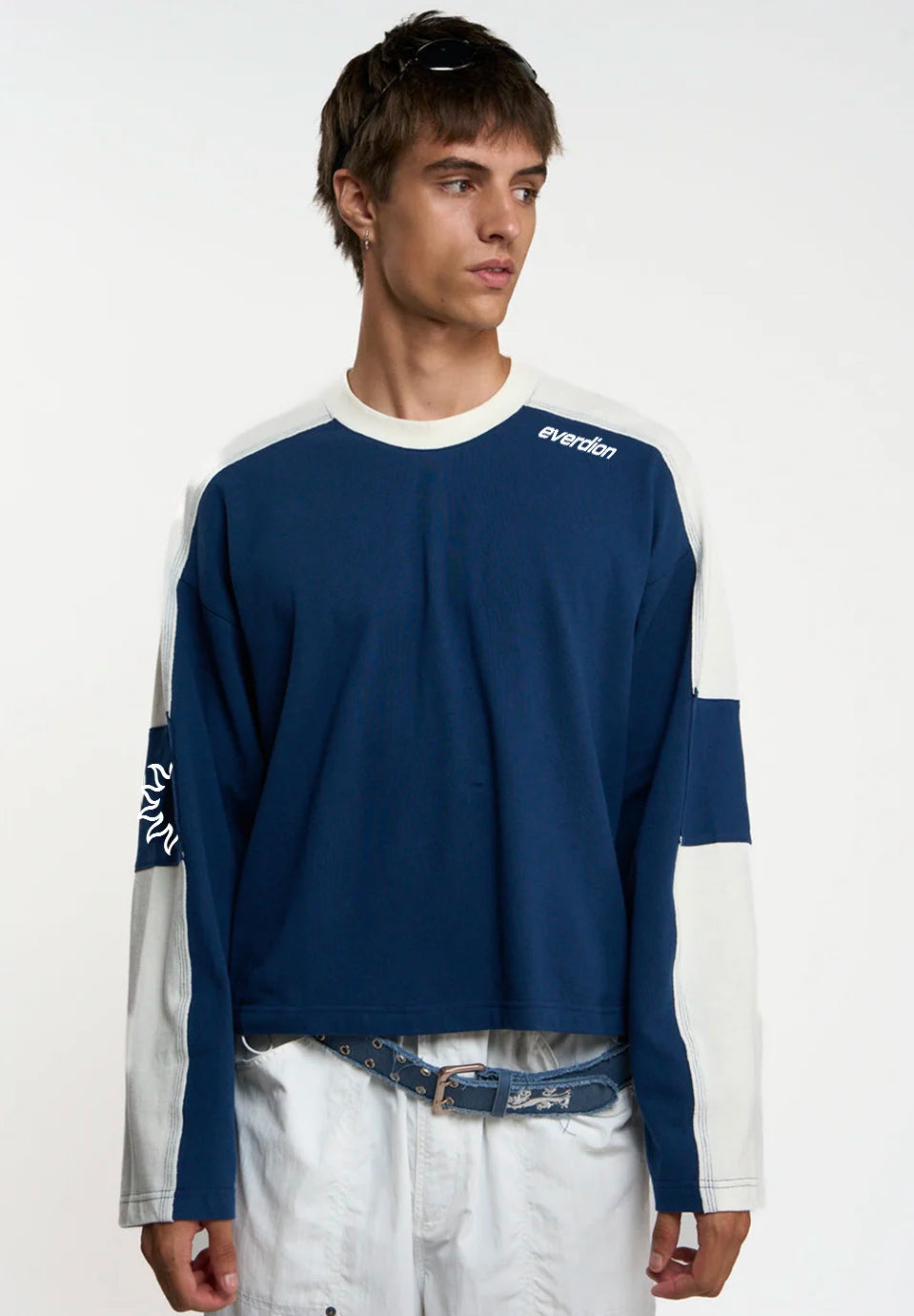 A man wearing a navy blue and white colorblock long-sleeve t-shirt with 'everdion' printed on the chest, paired with white pants and a denim belt, against a plain white studio background.