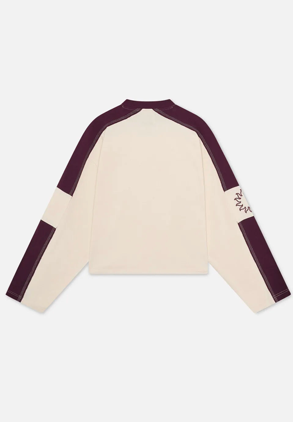 A long-sleeve raglan-style t-shirt laid flat on a light grey background, featuring an off-white body with dark plum purple shoulder and sleeve panels, plus a small embroidered logo on the upper sleeve.