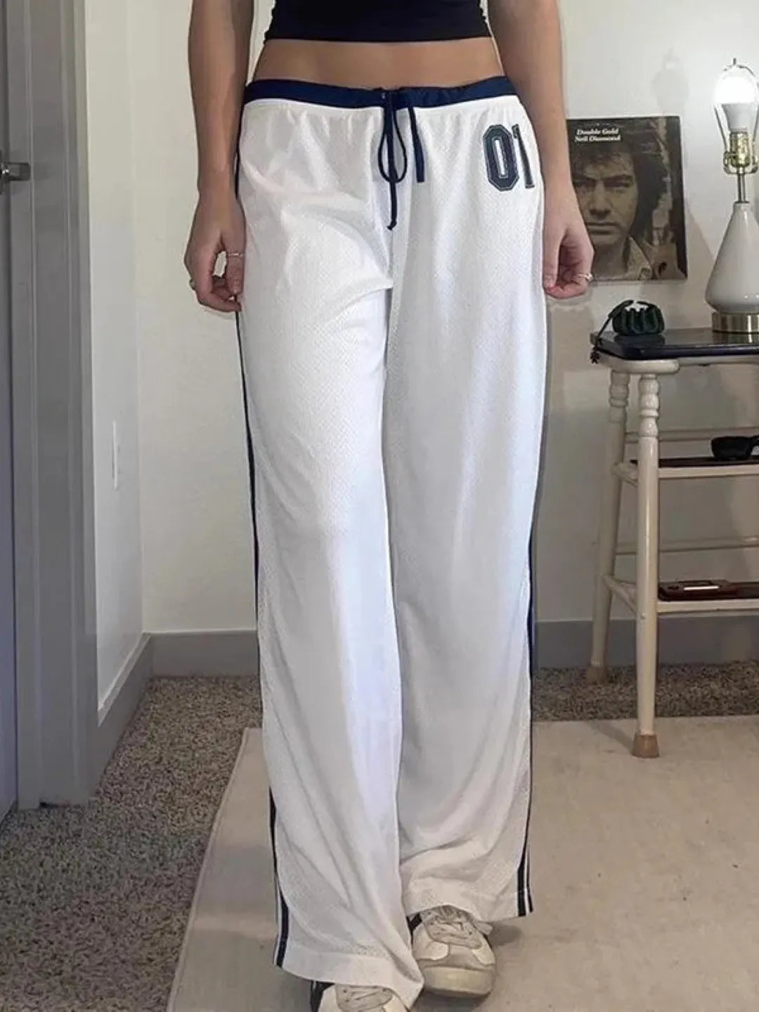 Person wearing white track pants with navy stripes indoors.