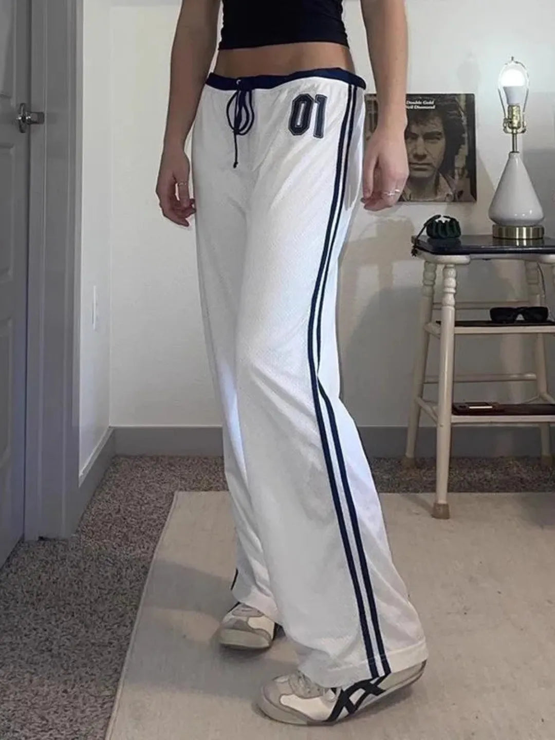 Person wearing white track pants with black stripes in a room.