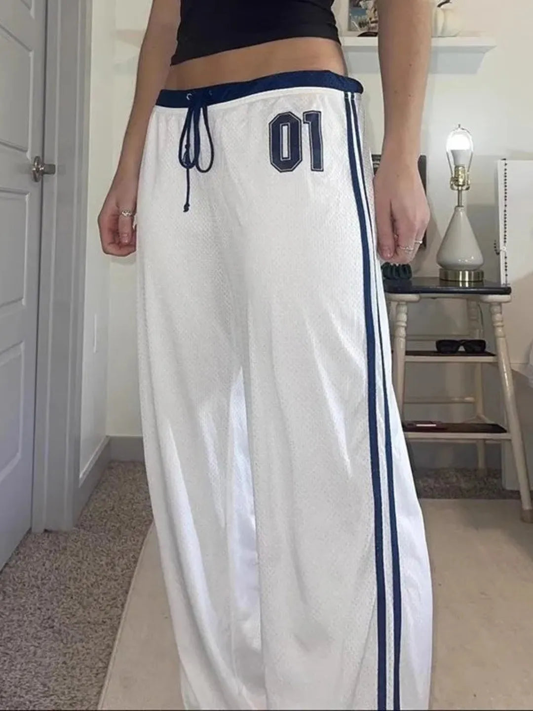 White track pants with blue stripes and numbering worn by a person indoors.