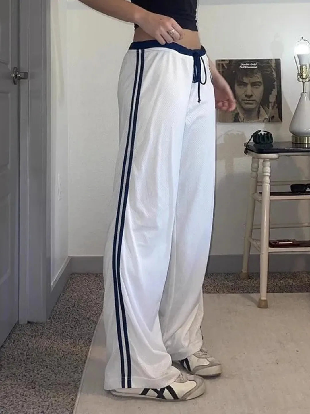 Person wearing white track pants with blue stripes in a room.
