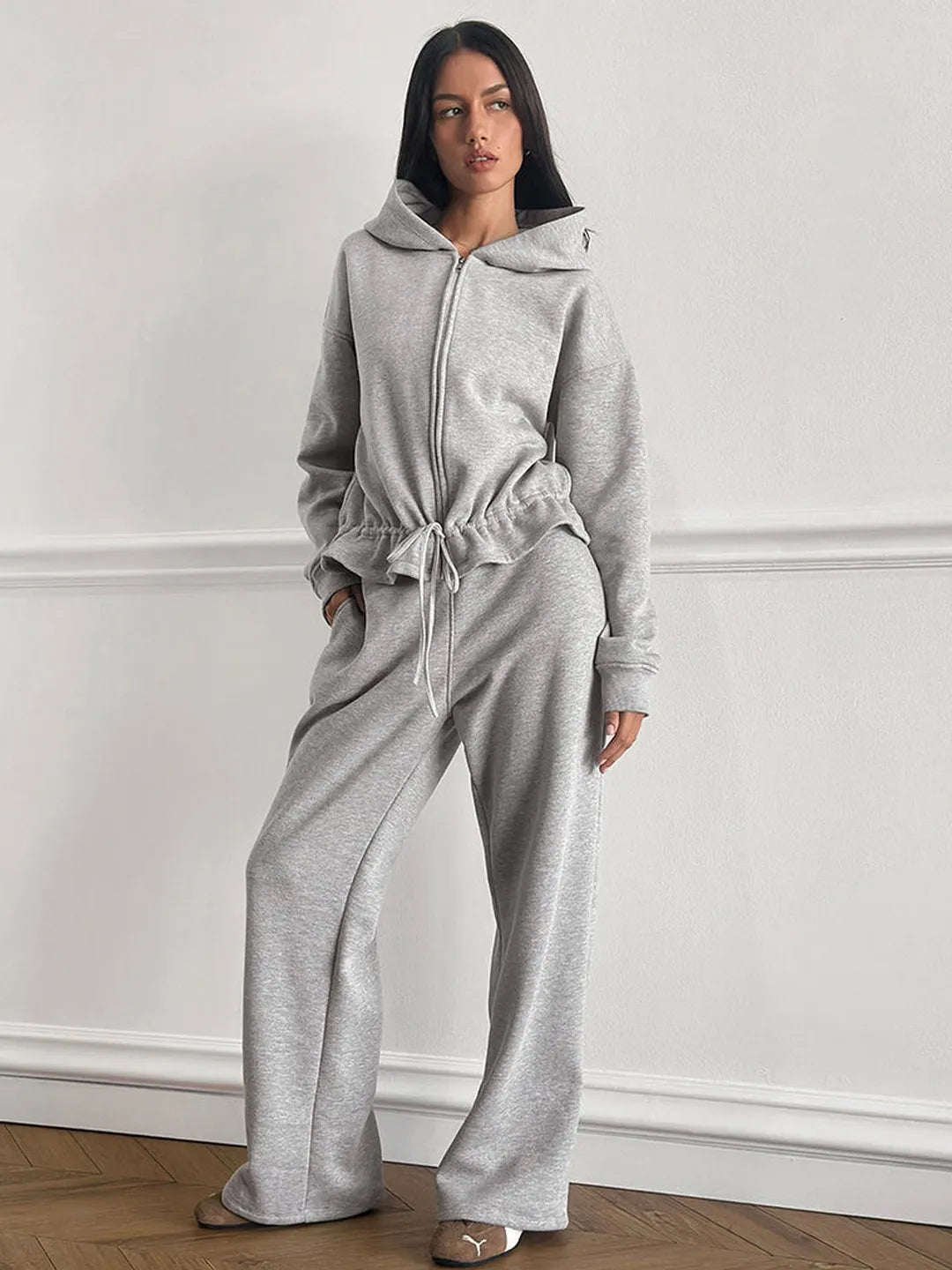 Person wearing a gray tracksuit against a white wall