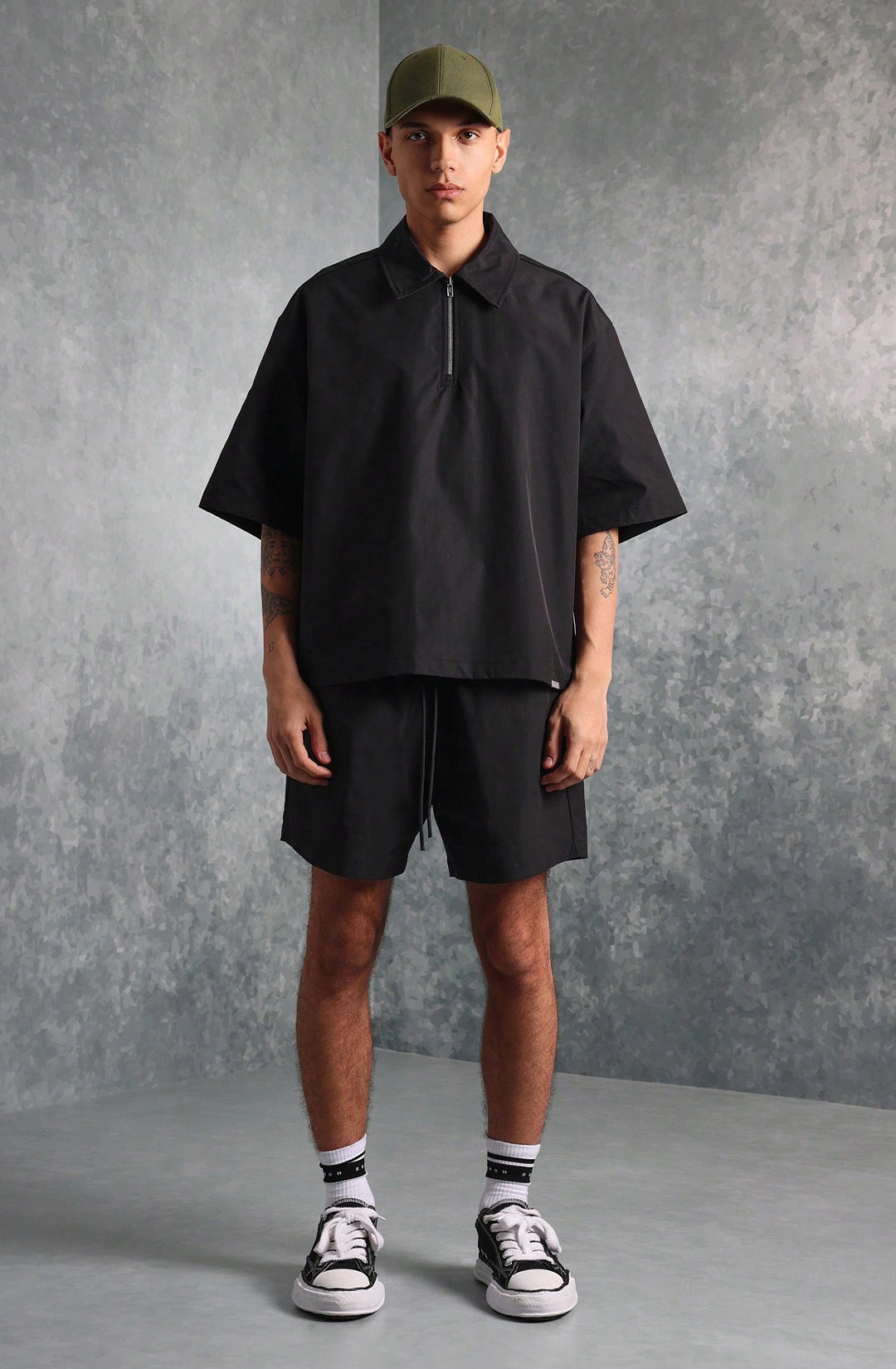 Person wearing a black outfit with a cap against a gray background