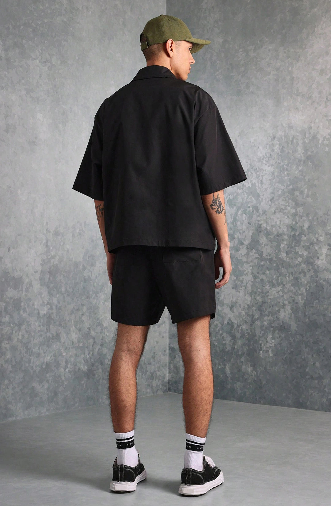 Person wearing a black shirt, shorts, and cap against a gray background