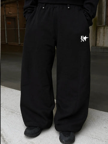 Black wide-leg sweatpants with a white 'EN' star logo on the left thigh, shown on a model in an urban setting.