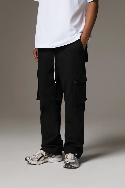 Person wearing black cargo pants and a white shirt on a plain background