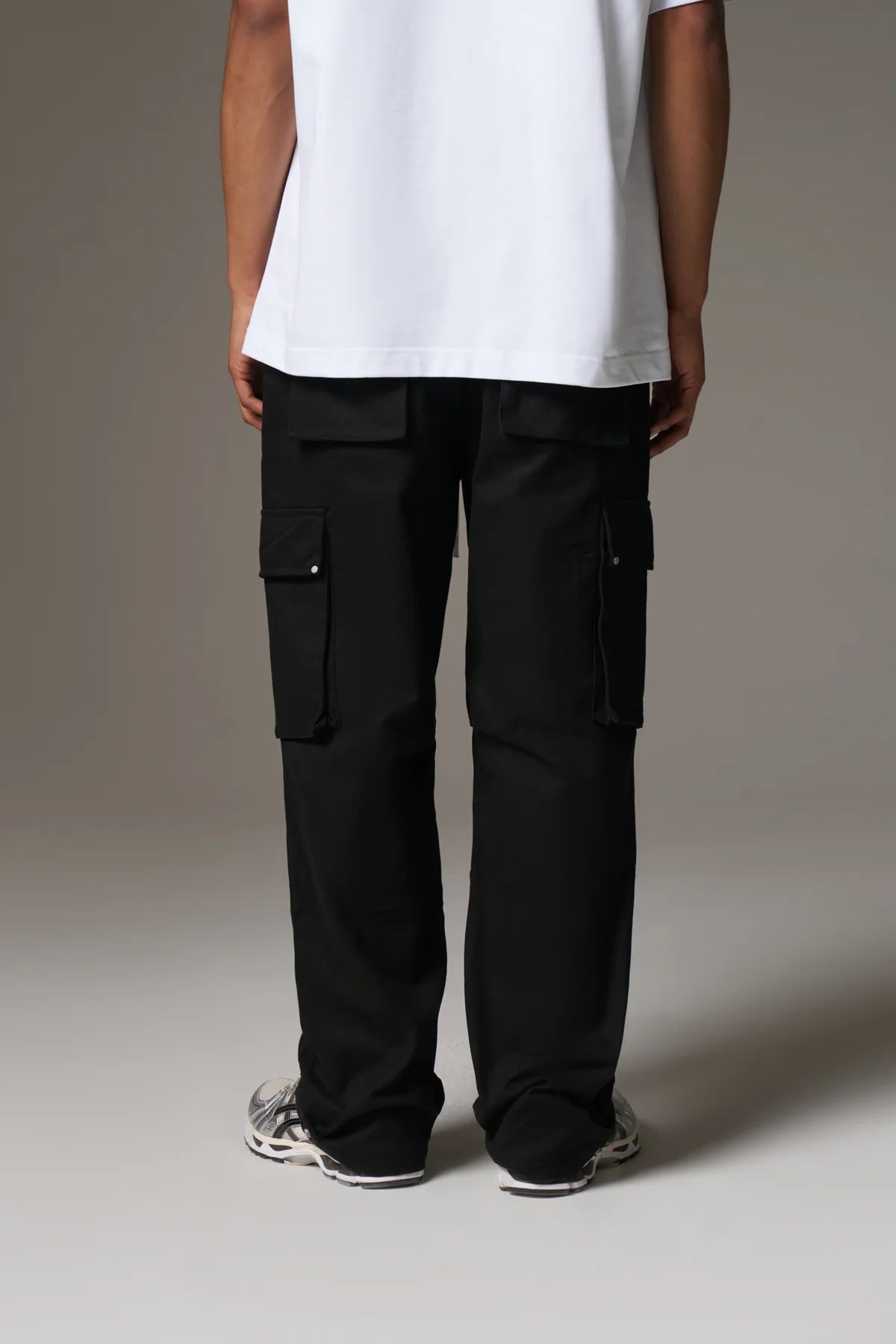 Person wearing black cargo pants and a white shirt on a neutral background