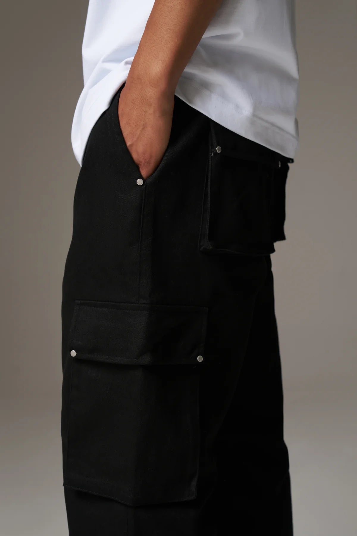 Person wearing black cargo pants with white shirt on a grey background