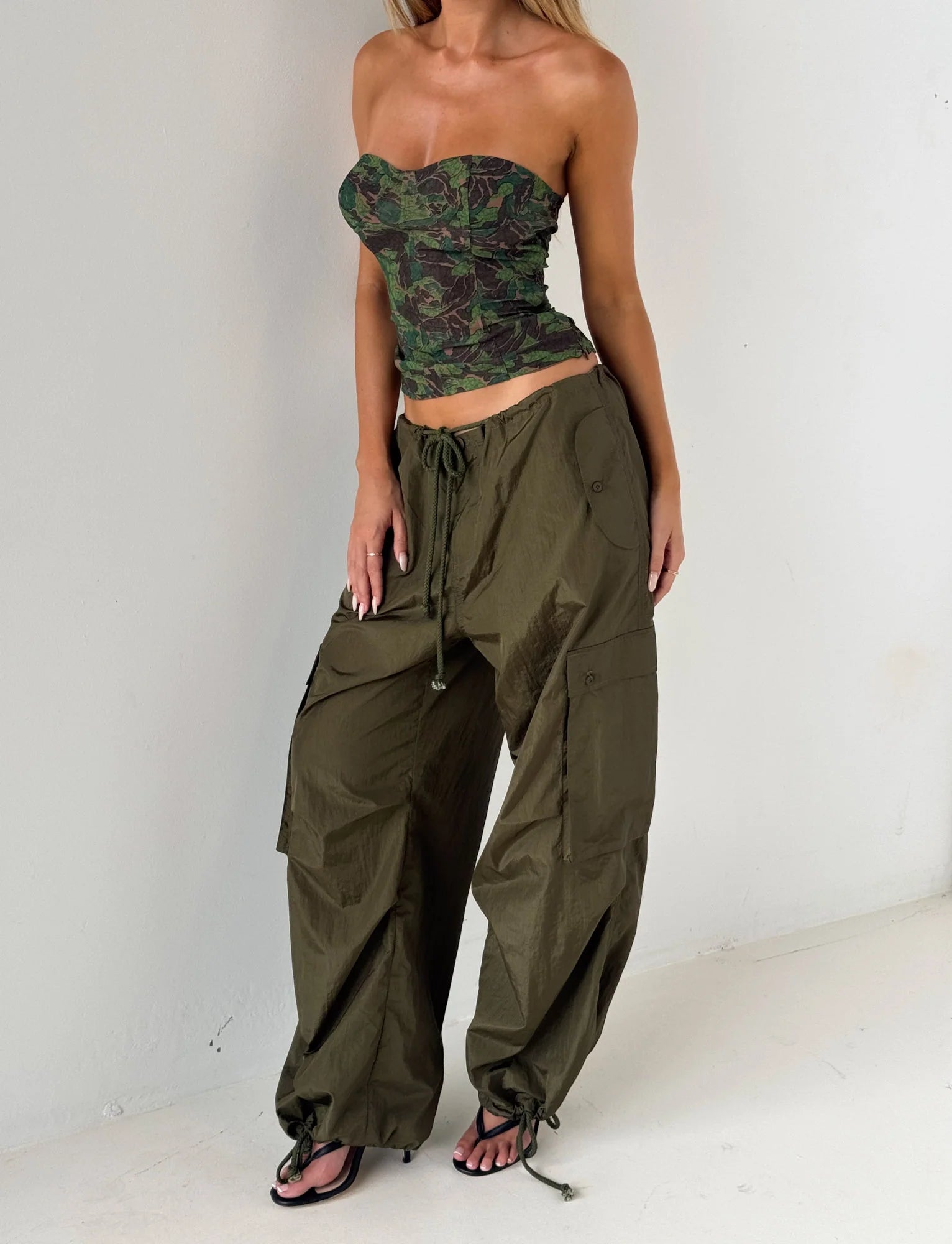Person wearing a camouflage top and olive green wide-leg pants on a white background