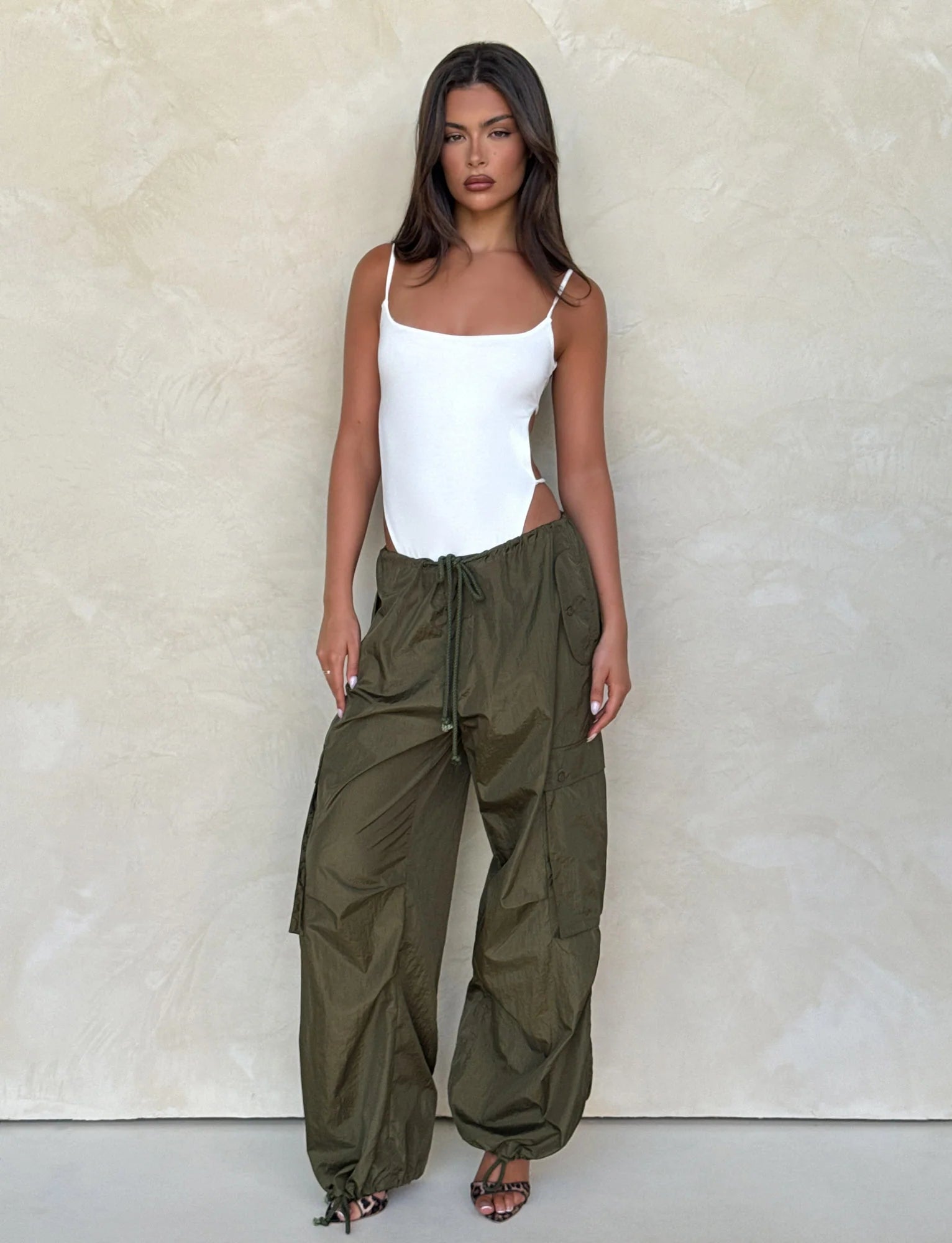 Woman wearing a white top and olive green pants against a neutral background