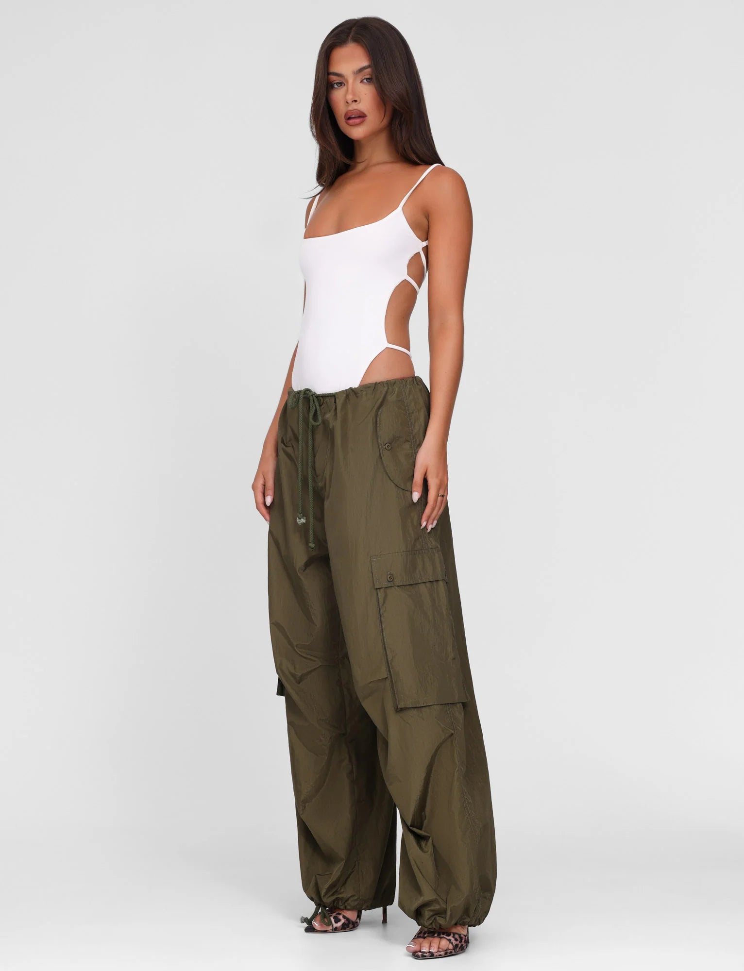 Woman wearing a white sleeveless top and olive green cargo pants on a white background